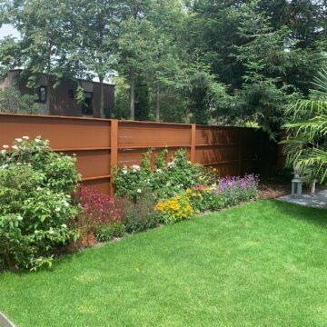 Cortenstalen schutting als moderne achterwand in tuin met groene beplanting ervoor